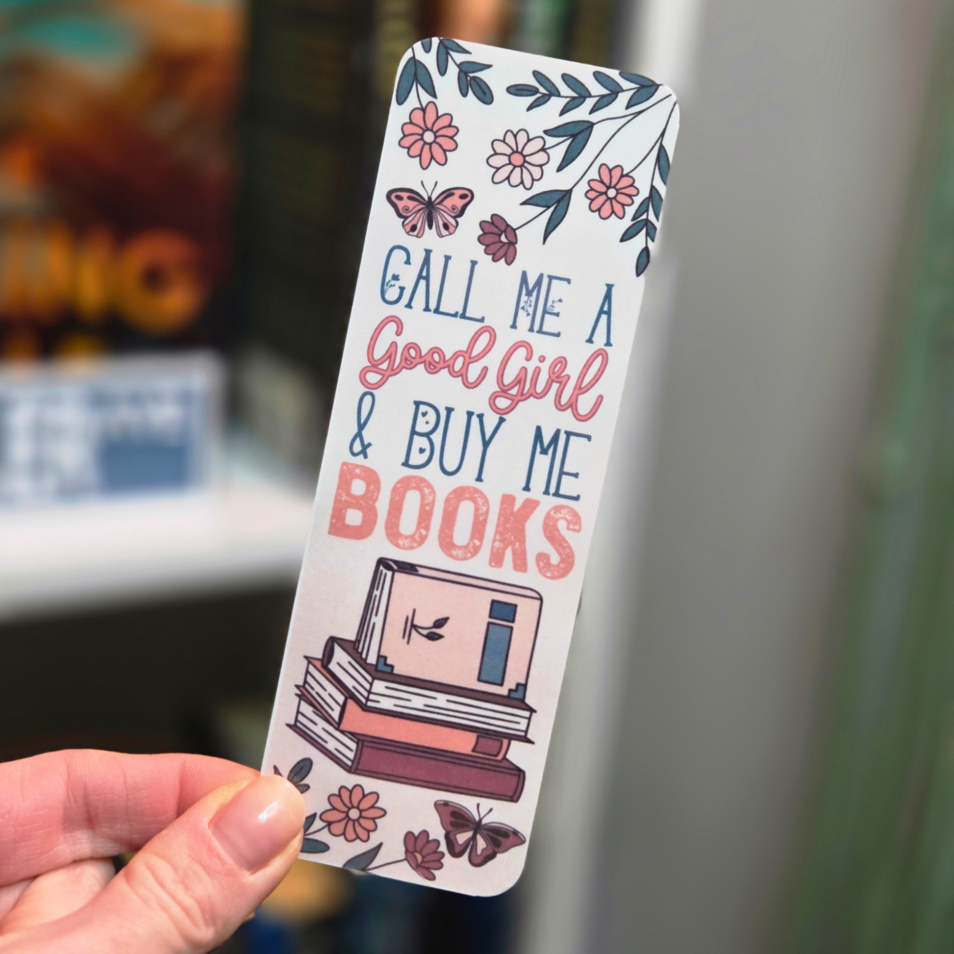 Bookmark with floral design and text held by a hand against a blurred background